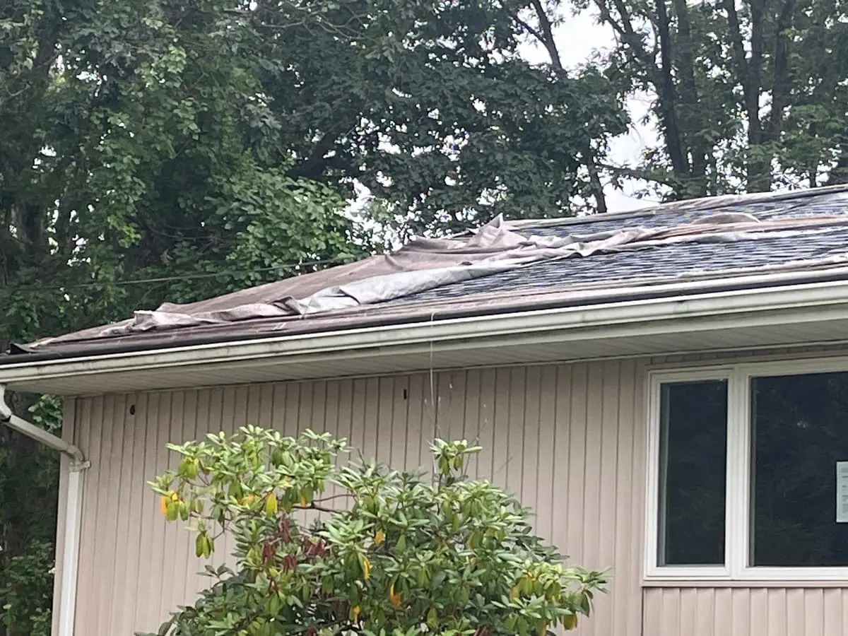 Selling a storm-damaged house in Bay Shore: torn roofing peeling off along the gutter line